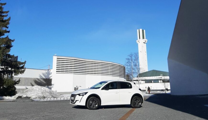 Valkoinen Peugeot e-208 Lakeuden Ristin ja vanhan kirjaston edessä kuvattuna.