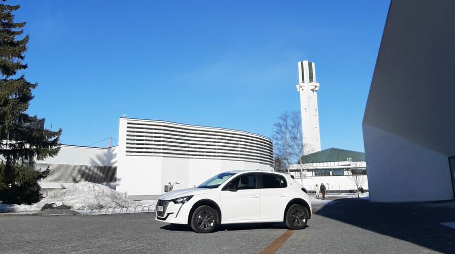 Valkoinen Peugeot e-208 Lakeuden Ristin ja vanhan kirjaston edessä kuvattuna.